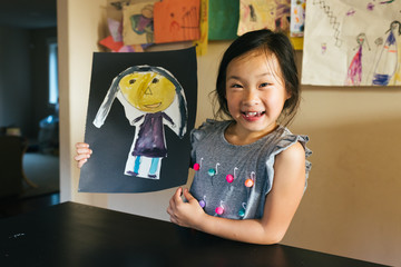 Young Asian American girl showing off self-portrait artwork