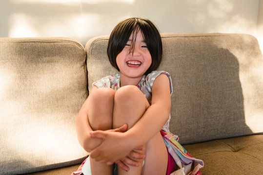 Asian American little girl laughing while clutching knees to chest