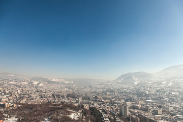 Aerial view of Sarajevo during a sunny winter afternoon, covered in snow. The historical center with its mosques and minarets can be seen in background