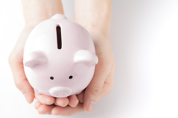 Top view of young female hands tender holding pink piggy bank on white table in soft tone, savings...