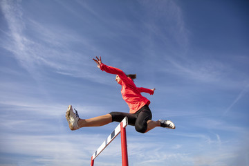 Female athlete jumping above the hurdle during the race