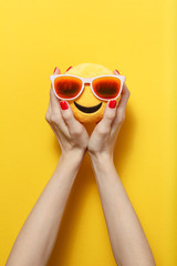 Hands holding the yellow toy with glasses on a bright yellow background