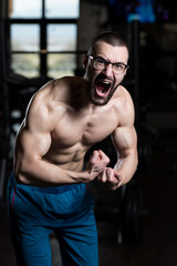 Fototapeta na wymiar Muscular Geek Man Flexing Muscles In Gym