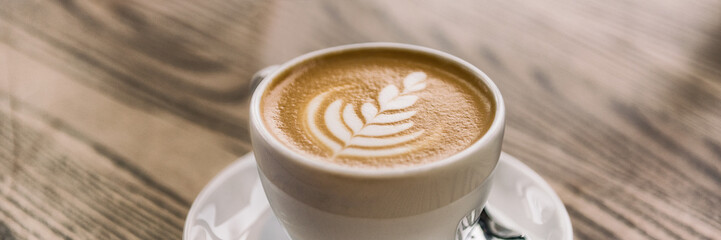 Coffee cup with latte art on cafe wood table banner panorama background.