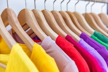 Fashion clothes hanging on clothing rack - bright colorful selection of clothes closet. Rainbow color choice of trendy girl outfits on hangers in store closet. Spring cleaning home wardrobe.