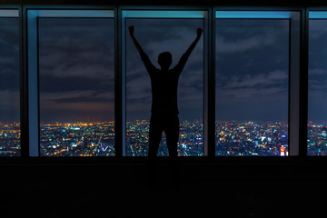 Man cheering while looking out large windows high above a sprawling city at night