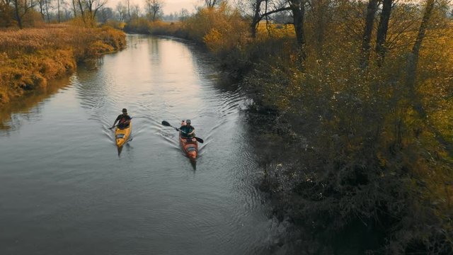 Medium aerial tracking shot of two kayakers paddling on calm river in beautiful nature.
