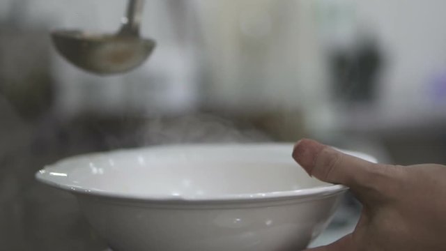 Closeup chef's hands pouring soup into the porcelain bowl - video in slow motion