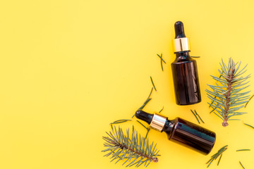 Pine essential oil in bottles on yellow background top view. Pattern with pine branch and cone copy space