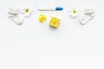 Pregnancy and preparation for childbirth. Pregnancy test near booties and flowers on white background top view copy space