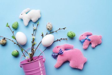 Top view of Easter eggs and handmade rabbits with spring twigs on a pastel blue background.
