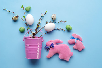 Top view of Easter eggs and handmade rabbits with spring twigs on a pastel blue background.