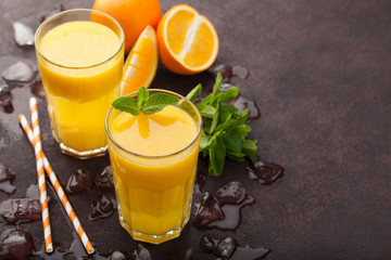 Two glasses of freshly squeezed orange juice and mint on a dark brown background. Top view with copy space