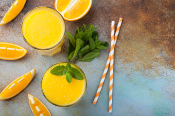 Two glasses with freshly squeezed orange juice and mint on an old rusty blue background. Top view with copy space