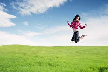 Carefree Asian woman making a big jump on meadow.