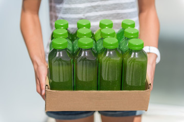 Green smoothie juice bottles box of cold pressed vegetable juices. Woman holding delivery box. Health trend for cleansing of organic raw juices. Juicing for diet cleanse detox.