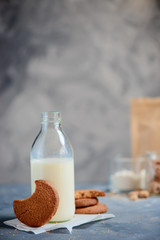 Cookie with a bite mark on a kitchen table with a milk bottle and baking ingredients out of focus. Tasty homemade pastry concept with copy space.