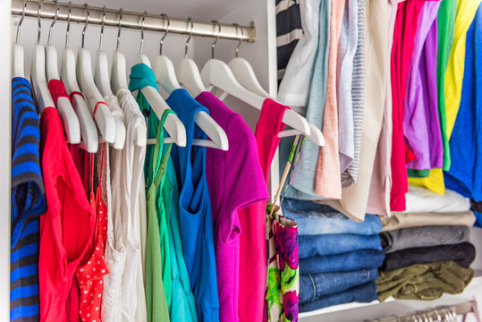 Fashion clothes in walk-in clothing closet or store display for shopping display. Colorful choices of trendy outfits well arranged in clean racks. Spring cleaning concept. Summer home living wardrobe.