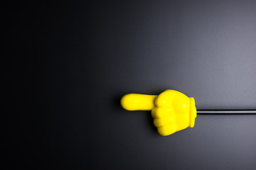 Yellow plastic hand pointing on black background with copy space.