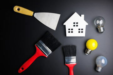 White house toy and paint brush, painters equipment on black background with copy space.Real estate concept, New house concept, Finance loan business concept, Repair maintenance concept.