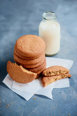 Cookies with bite marks and a bottle of milk on a light blue kitchen table with copy space. Healthy breakfast minimalist concept.