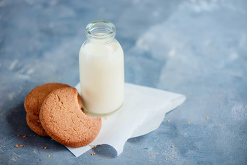 Cookies with bite marks and a bottle of milk on a light blue kitchen table with copy space. Healthy breakfast minimalist concept.