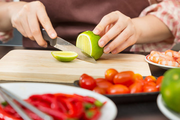 Female hands cutting green lime on wooden cutting board in her home kitchen
