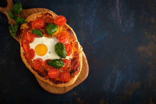 Homemade tasty pizza with egg, cheese, tomatoes and basil.