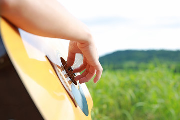 Hand playing on acoustic guitar in the nature.

