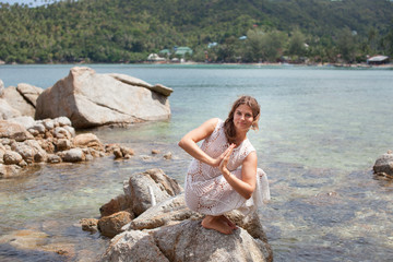 Woman doing yoga tree pose namaste on the stone near the ocean