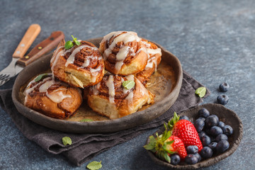 Homemade cinnamon buns in glaze on a dark plate with berries, dark background, copy space. Breakfast dessert concept.