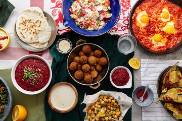 Overhead image of traditional jewish and middle eastern food: falafel, fattoush, tabouli, shakshuka, balila, hummus, roasted eggplants and spicy beetroot dip. Israeli cuisine concept