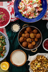 Overhead image of traditional jewish and middle eastern food: falafel, fattoush, tabouli, shakshuka, balila, hummus, roasted eggplants and spicy beetroot dip. Israeli cuisine concept