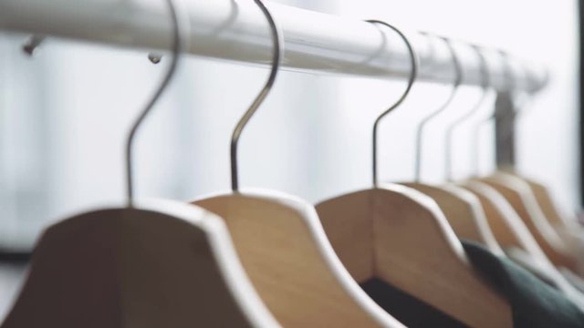 On the floor stand (rave) for clothes hanging wooden hangers with things. Hanger with women's clothes of different colors against the background of a panoramic window, close-up. Woman wardrobe.