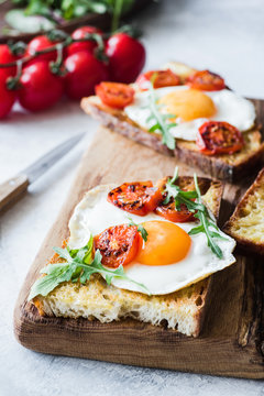 Breakfast toast with egg, arugula and roasted tomato, closeup view. Vertical