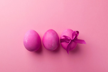 Bright pink eggs with a satin bow on a trendy violet background. Celebratory concept.