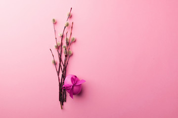 Bright violet egg with a satin bow and pussy-willow branches on a trendy pink background.