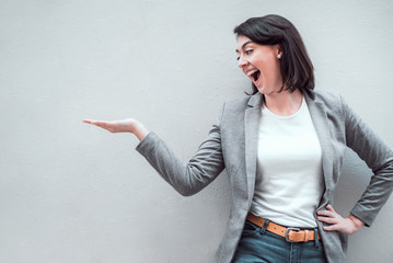 Smiling happy businesswoman is showing something or some product on gray wall with copy space 