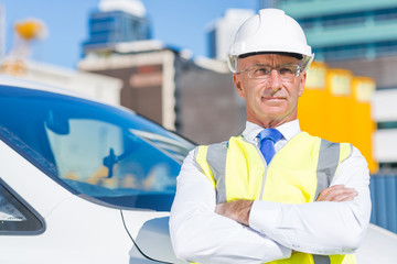 Senior builder man outdoors at construction site near his car looking in camera