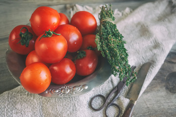 Tomatoes on a beautiful old metal plate with a thyme with a knife and scissors on a wooden table in a rustic style. Copy space.