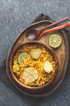 Curry bulgur with vegetables in wooden bowl. Dark background, top view, vegan meal concept.