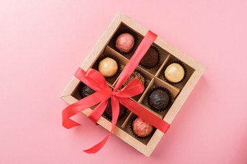 A set of assorted chocolates in a paper box with a satin pink ribbon on a pastel background.Flat...