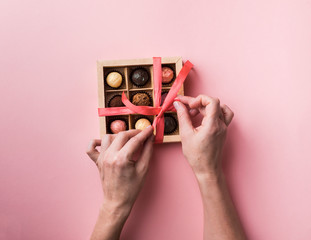 Les mains féminines attachent un arc d& 39 un ruban de satin sur une boîte avec un ensemble de chocolats. Fond rose tendance.