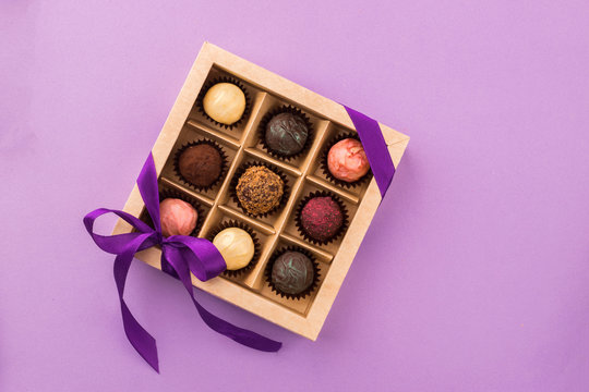 A set of assorted chocolates in a paper box with a satin purple ribbon on a bright background