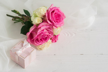  Fresh pink roses and a gift in a pink little box on a white background decorated with a transparent cloth