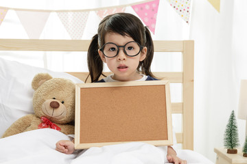 Child girl holding blank board on the wooden bed in her bedroom, Space for your text