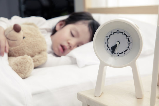 Child girl sleeping with alarm clock on the wooden bed in her bedroom, Happy asian child little girl and alarm clock wake up in the morning