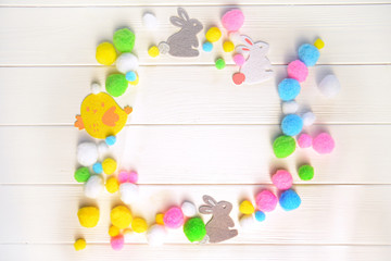 Round multicolor frame from woolen easter bunnies, chick and eggs on the white wooden background. Top view, flat lay, copy space