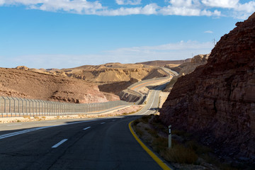 Asphalt road and fence wall on boarder with Egypt in desert Negev, Israel, road 12, transport infrastructure in desert, scenic mountains route from Eilat to north of Israel