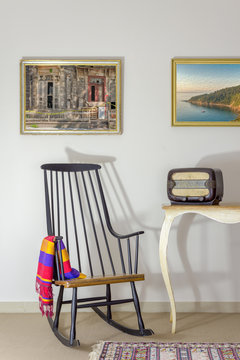 Interior shot of vintage rocking chair and old radio on old style vintage table on background of off white wall with two hanged paintings including clipping path for paintings